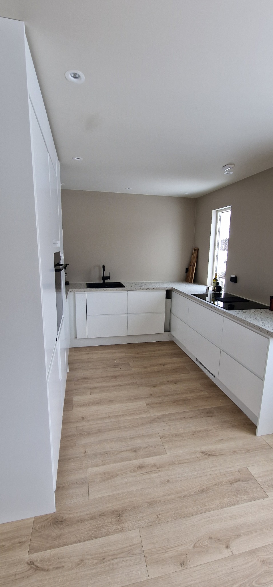 Nowoczesna, jasna kuchnia w Opolu z białymi szafkami i drewnianą podłogą. Minimalistyczny design, czarny zlew i płyta indukcyjna. Stonowana kolorystyka ścian.