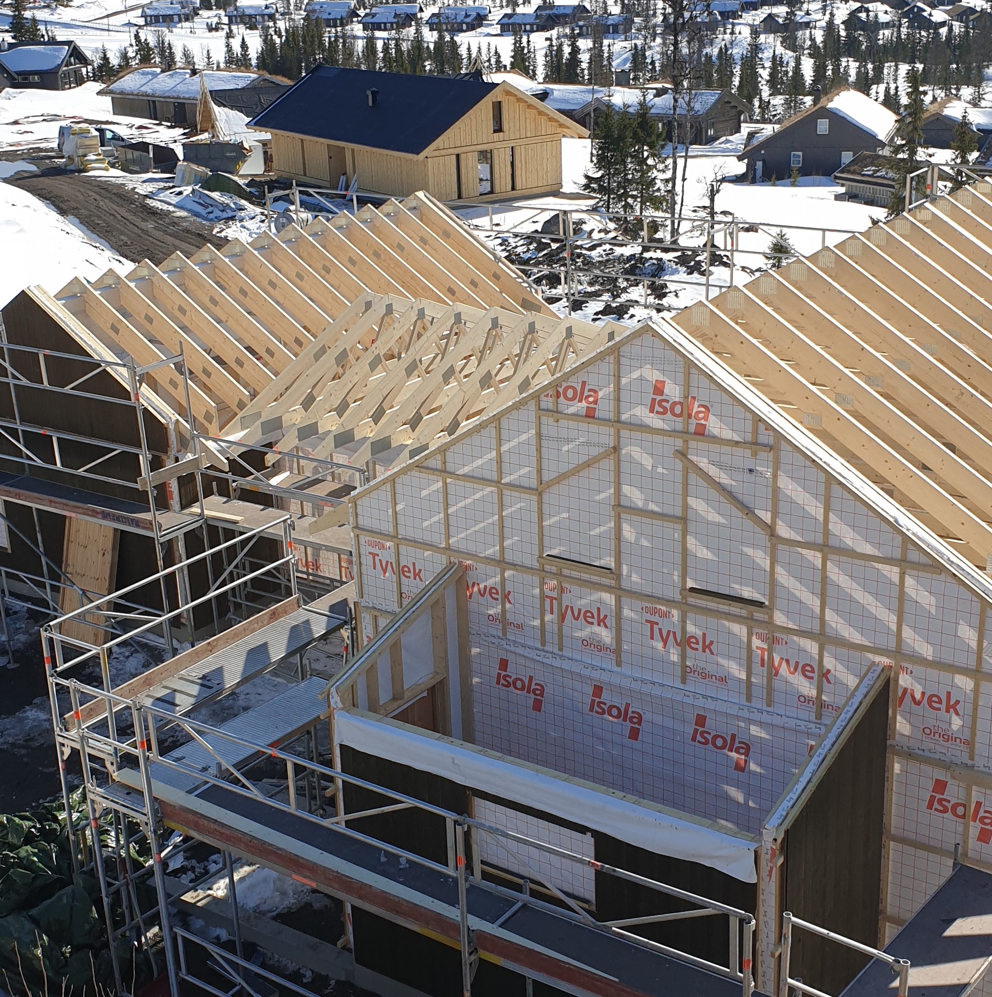 Budowa domu w zimowym krajobrazie: szkielet drewniany, rusztowania, membrany izolacyjne Tyvek i Isola. Widok z góry na plac budowy z konstrukcją dachu.