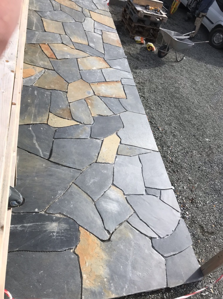 Ułożona posadzka z nieregularnych, szarych płyt kamiennych z beżowymi akcentami. W tle widoczne narzędzia i gruz.
