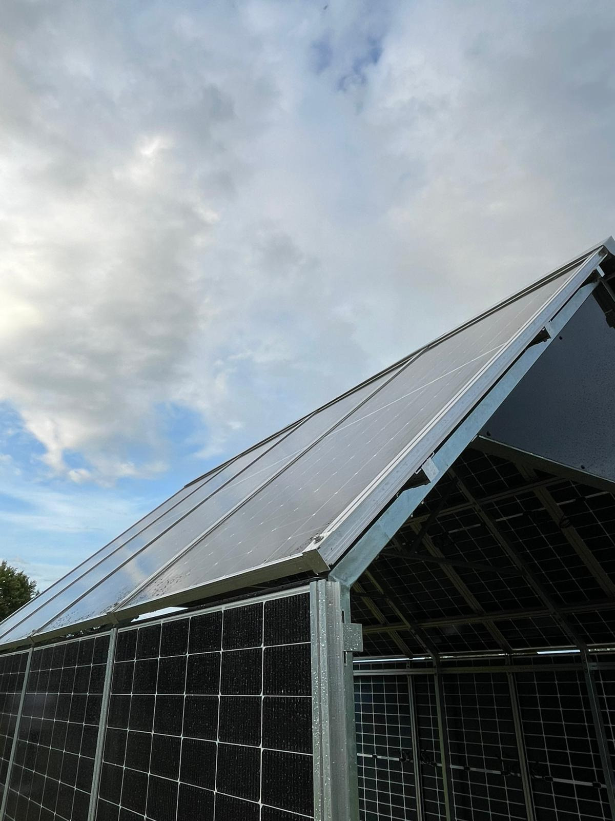 Konstrukcja szkieletowa z panelami solarnymi na dachu w pochmurny dzień. Widok z dołu ukazuje detale metalowej ramy i modułów fotowoltaicznych.