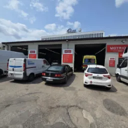 Warsztat samochodowy MOTRIO z zaparkowanymi pojazdami: karetka, Volkswagen Phaeton, Toyota Yaris. W tle budynek firmy LALAK Development.