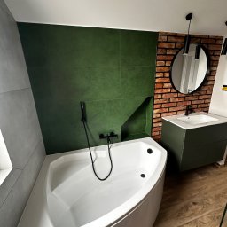 ProF-Bud - Nowoczesna łazienka z narożną wanną, zielonymi płytkami i ścianą z cegły. Czarna armatura i okrągłe lustro dodają elegancji. Drewnopodobna podłoga.