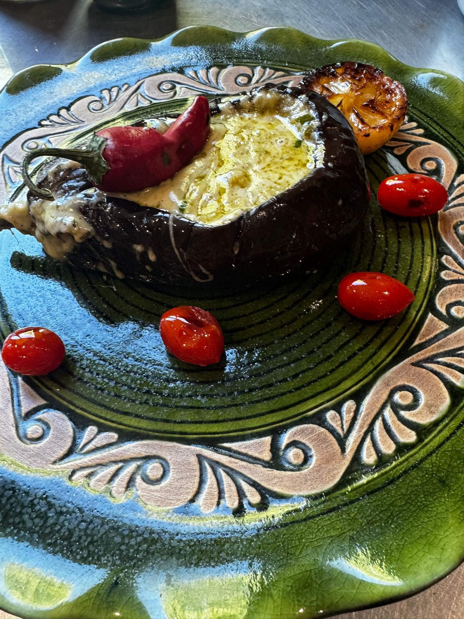 Faszerowany bakłażan z papryczką chili na zielonym talerzu z pomidorkami koktajlowymi, oświetlony ciepłym światłem, prezentowany jako danie cateringowe.