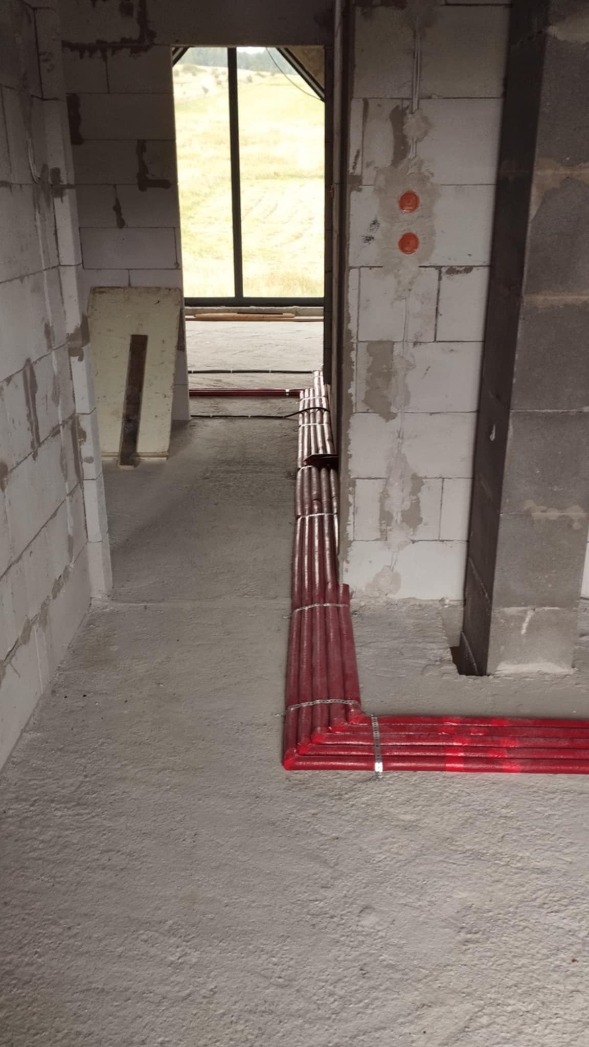 Czerwone rury ogrzewania podłogowego, ułożone w surowym stanie, przed wylaniem posadzki, widoczne ściany z pustaków.