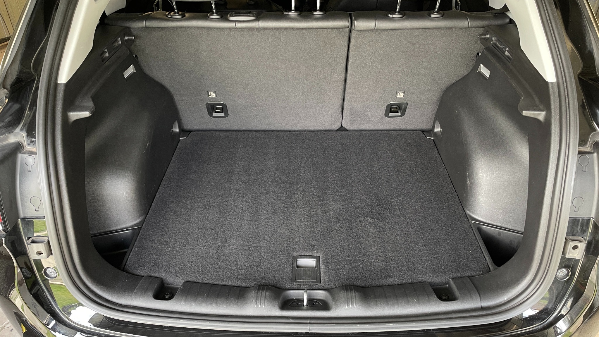 Czysty, pusty bagażnik czarnego samochodu typu SUV z widoczną szarą wykładziną. Widoczne elementy mocujące i tylne siedzenia.