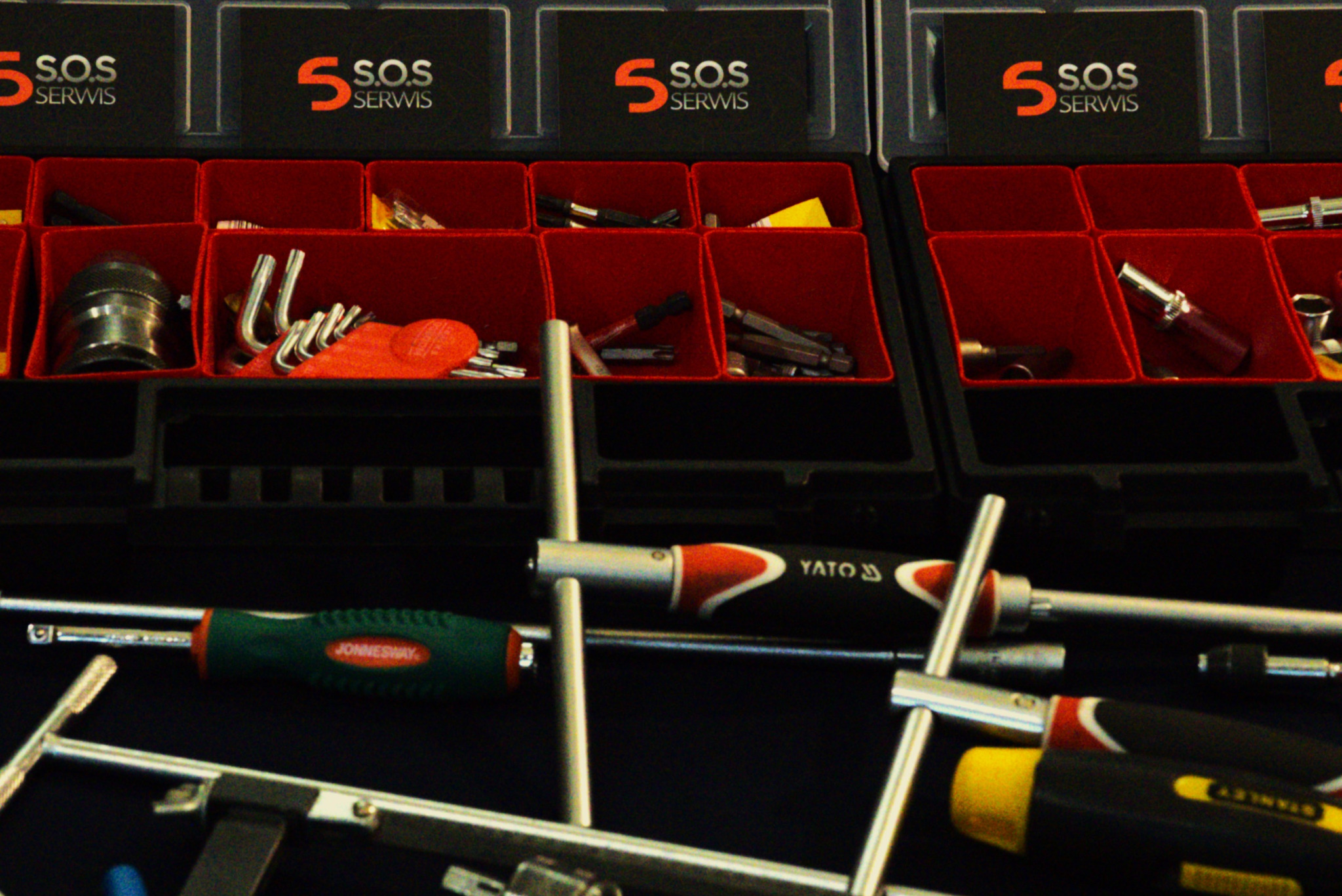 Otwarty organizer z narzędziami: klucze, nasadki, bity i wkrętaki marek Yato, Jonnesway i Stanley. Widoczne logo 'S.O.S Serwis' na przegródkach.