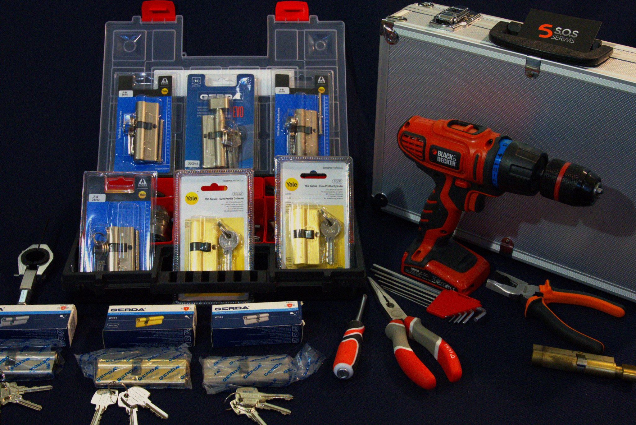 Zestaw ślusarski z wiertarką Black&Decker, narzędziami Yato, zamkami Gerda i Yale, oraz metalową walizką serwisową na ciemnym tle.