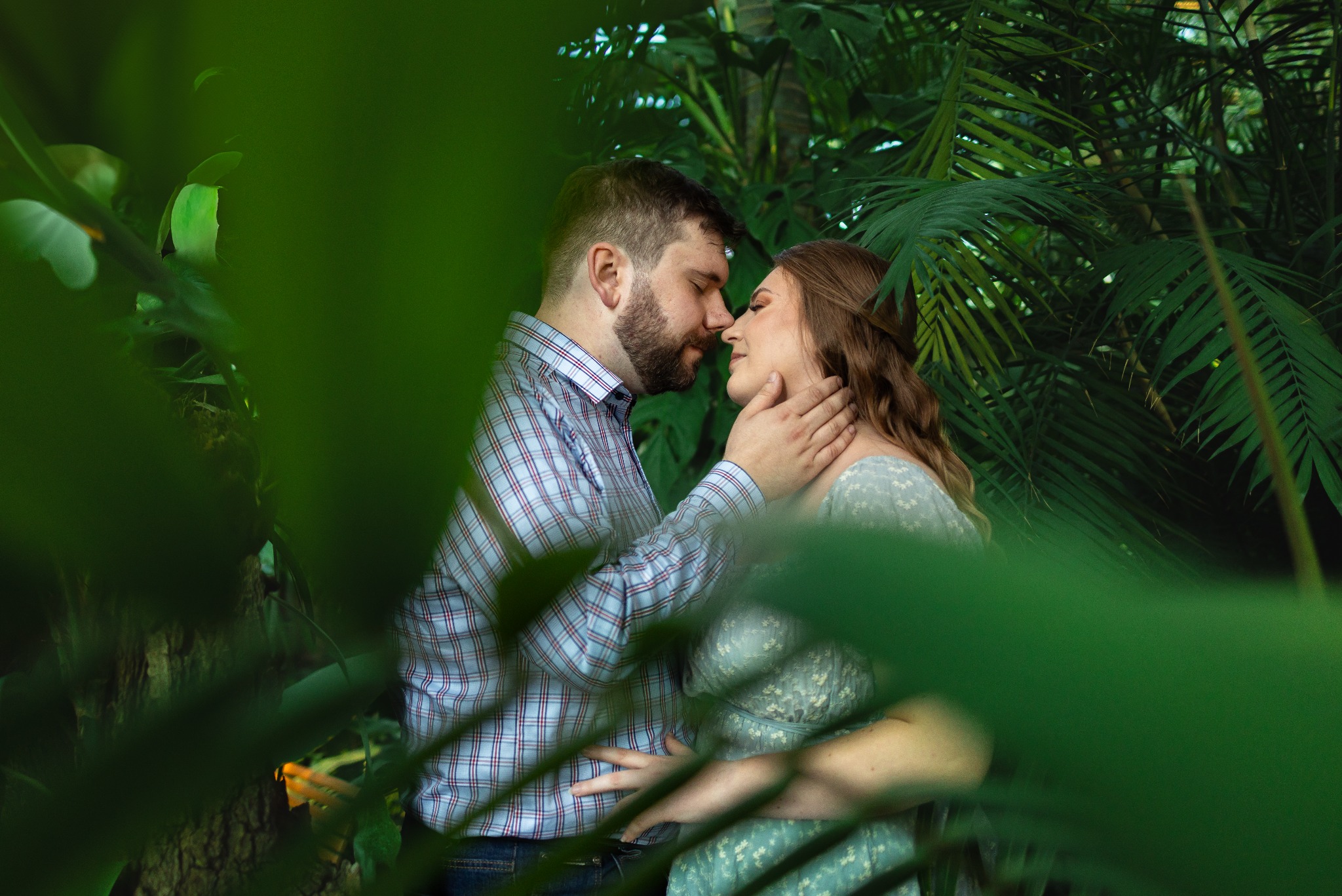 Zakochana para w naturalnym otoczeniu tropikalnej roślinności, delikatne dotknięcie nosami, intymna chwila uchwycona przez obiektyw fotografa.