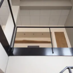 Nowoczesna, czarna balustrada metalowa wewnątrz budynku, widok z dołu, z elementami drewnianymi w tle. Minimalistyczny design, stonowana kolorystyka.