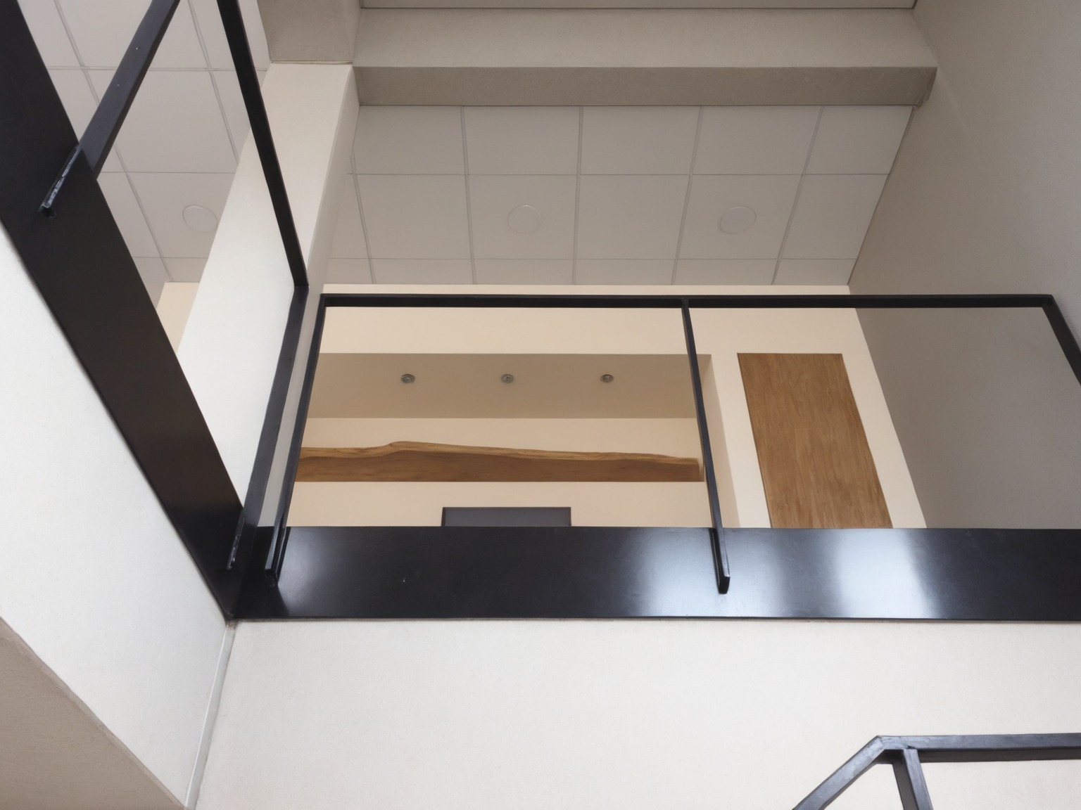 Nowoczesna, czarna balustrada metalowa wewnątrz budynku, widok z dołu, z elementami drewnianymi w tle. Minimalistyczny design, stonowana kolorystyka.