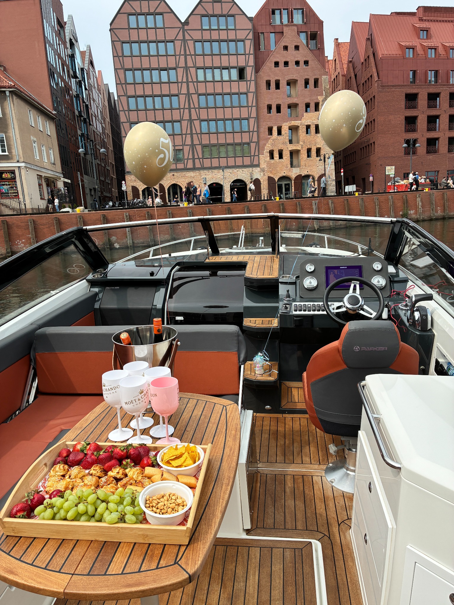 Luksusowy jacht z przekąskami i szampanem na tle malowniczego nabrzeża w Gdańsku, z dekoracyjnymi balonami, sugerujący ekskluzywną imprezę na wodzie.