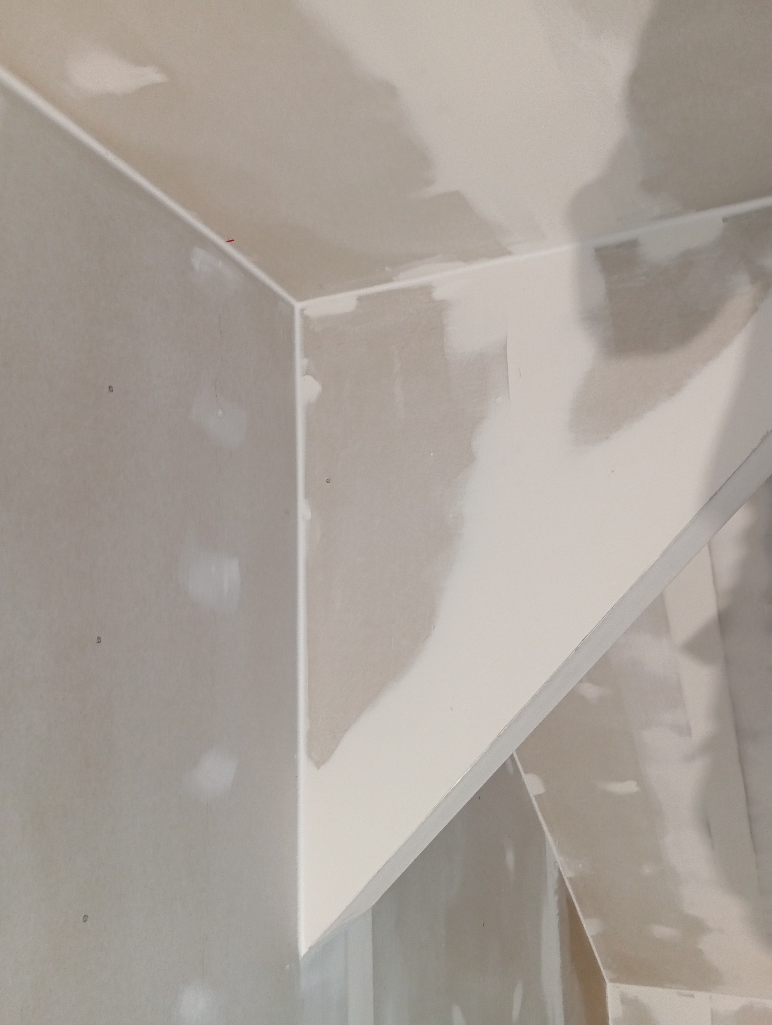 Fragment wnętrza w trakcie prac wykończeniowych: połączenie płyt gipsowo-kartonowych na suficie i ścianach, widoczne miejsca szpachlowania.