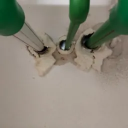 Świeżo uszczelnione pianką montażową, zielone rury instalacyjne wystające ze ściany. Widoczne otwory w ścianie i fragment białej instalacji elektrycznej.