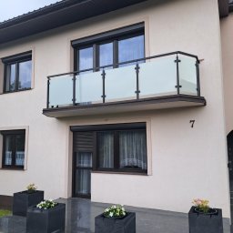 AP-STAL - Elegancka balustrada balkonowa ze szkła i czarnych elementów, widoczna z zewnątrz budynku. Nowoczesny design z numerem domu '7'.