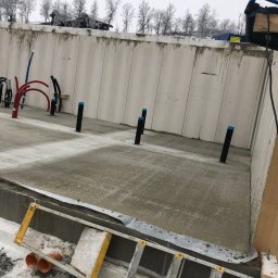 GDM CONSTRUCTION GRZEGORZ DZIADOWIEC - Zalany fundament budynku żelbetowego z wystającymi rurami instalacyjnymi. W tle ściany szalunkowe i zimowy krajobraz. Na pierwszym planie drabina.