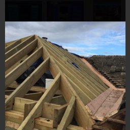 GDM CONSTRUCTION GRZEGORZ DZIADOWIEC - Drewniana konstrukcja dachu w trakcie budowy, widoczne krokwie i łaty, częściowo pokryte folią. W tle fragment istniejącego dachu z dachówką.