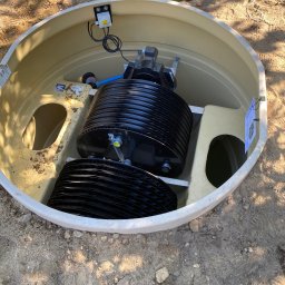 GDM CONSTRUCTION GRZEGORZ DZIADOWIEC - Wnętrze beżowego zbiornika oczyszczalni ścieków z czarnymi elementami filtracyjnymi, widoczne przewody i pokrywa obok. Ziemiste tło.