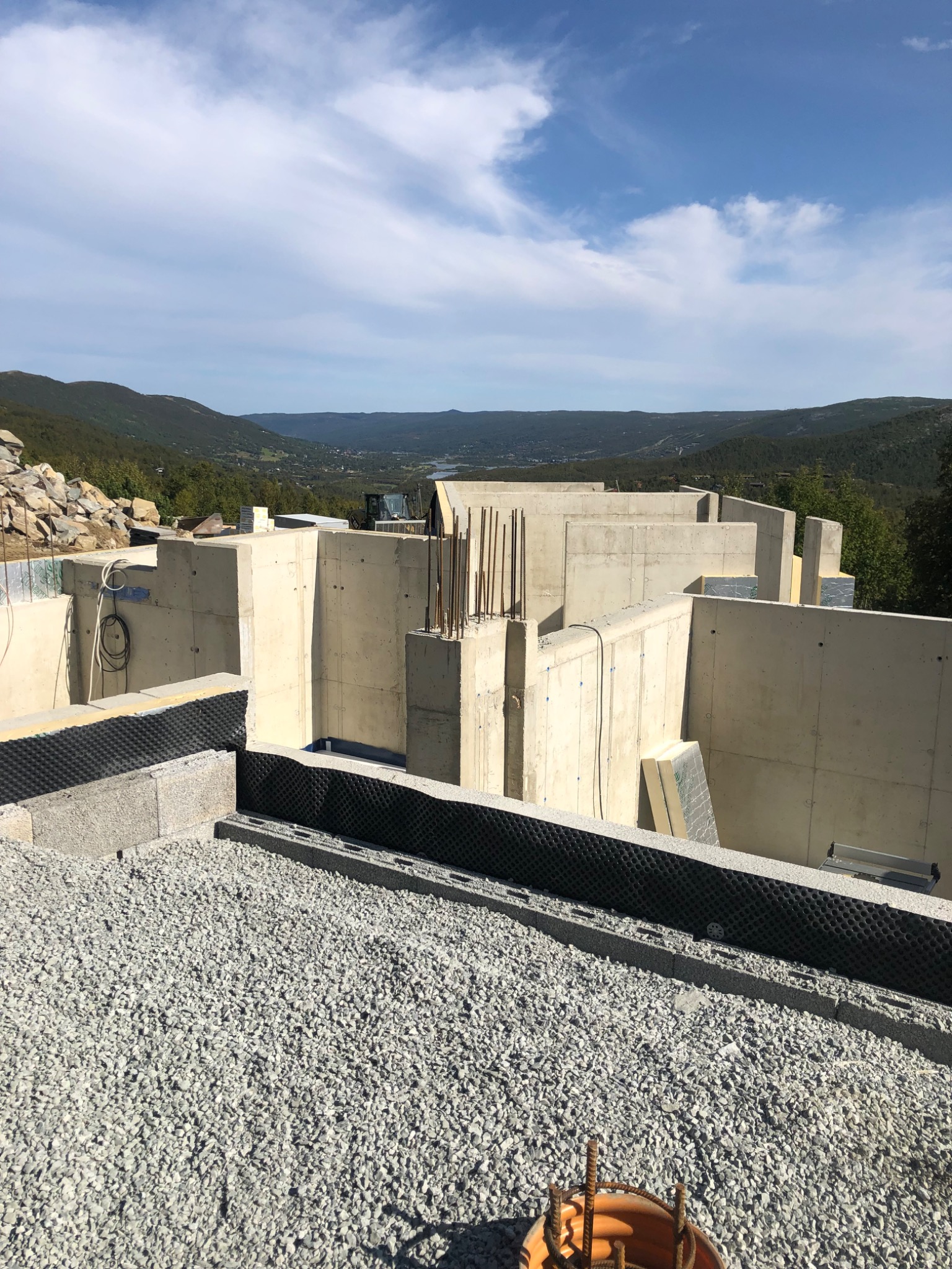 Betonowe fundamenty domu w trakcie budowy, widok z góry na otoczenie górskie i błękitne niebo z chmurami, zbrojenia, izolacja przeciwwilgociowa.