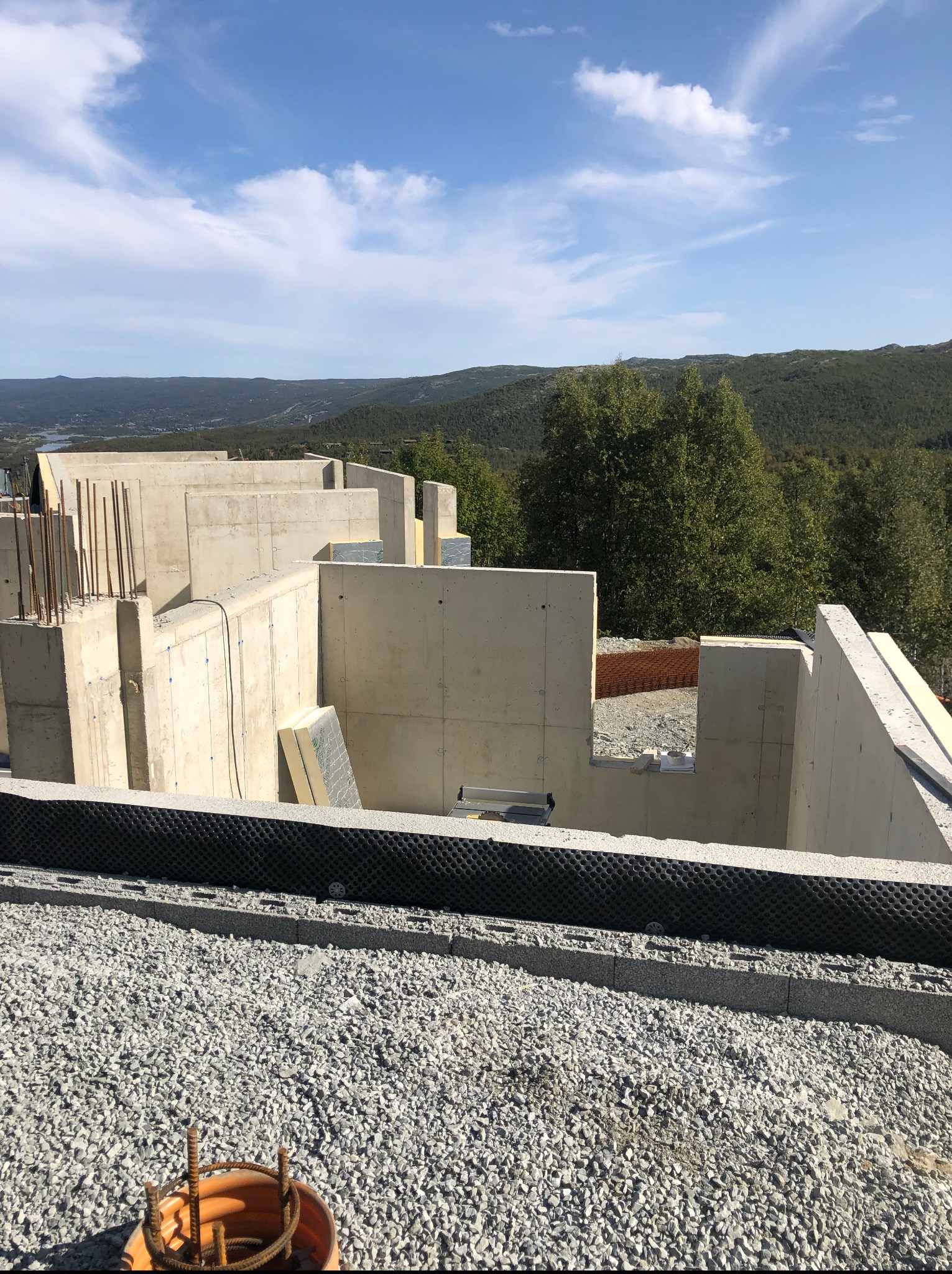 Surowa, betonowa konstrukcja fundamentów domu na tle górskiego krajobrazu. Widoczne zbrojenia i izolacja, etap budowy w słoneczny dzień.