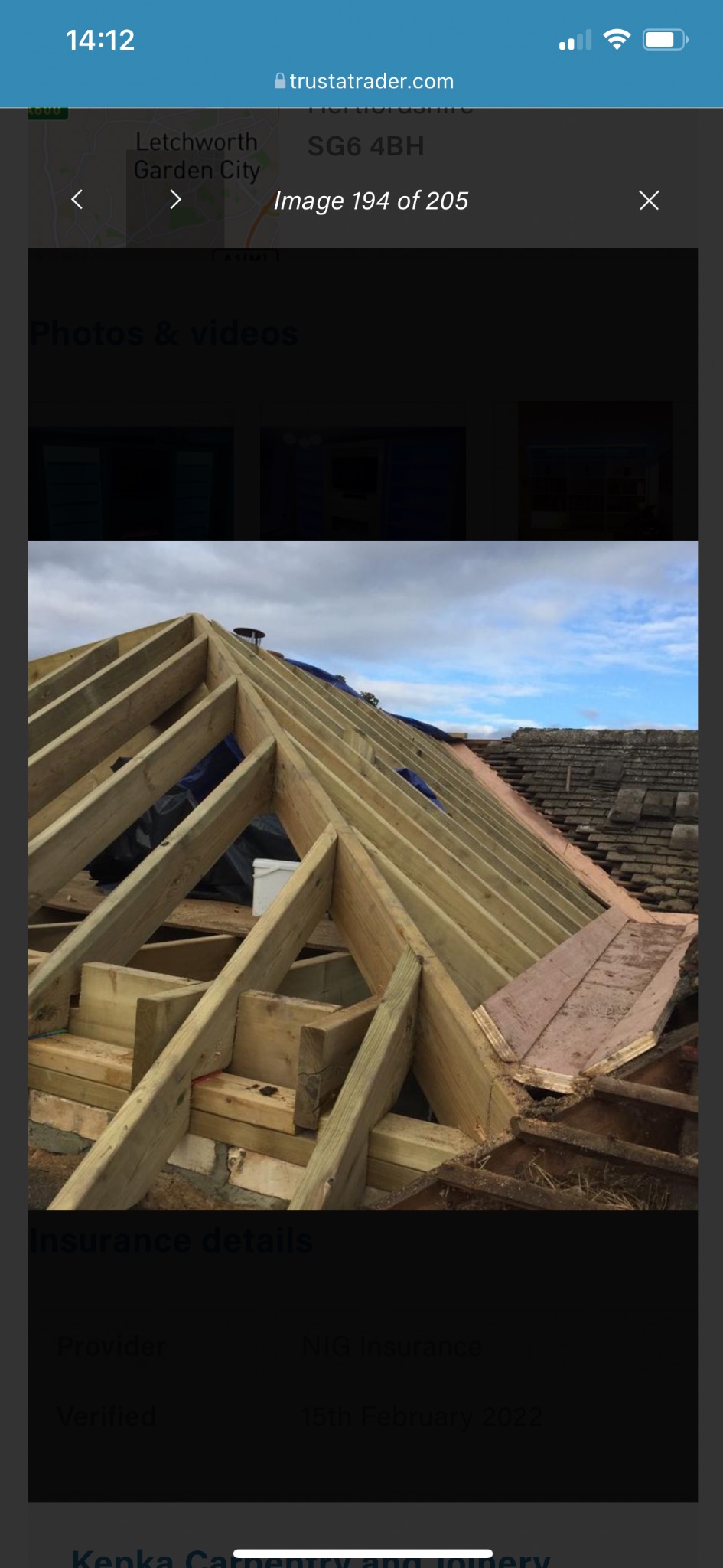 Drewniana konstrukcja dachu w trakcie budowy, widoczne krokwie i łaty, częściowo pokryte folią. W tle fragment istniejącego dachu z dachówką.