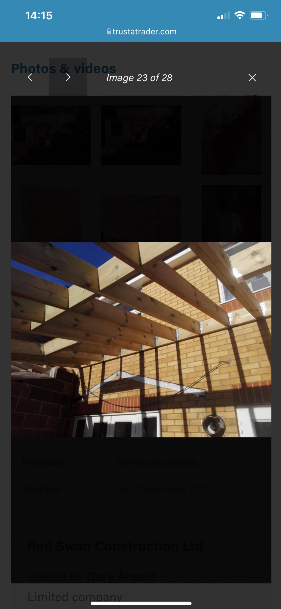 Drewniana konstrukcja z belek na tle ceglanego budynku i błękitnego nieba. Widoczne metalowe łączniki. Etap budowy zadaszenia tarasu lub werandy.