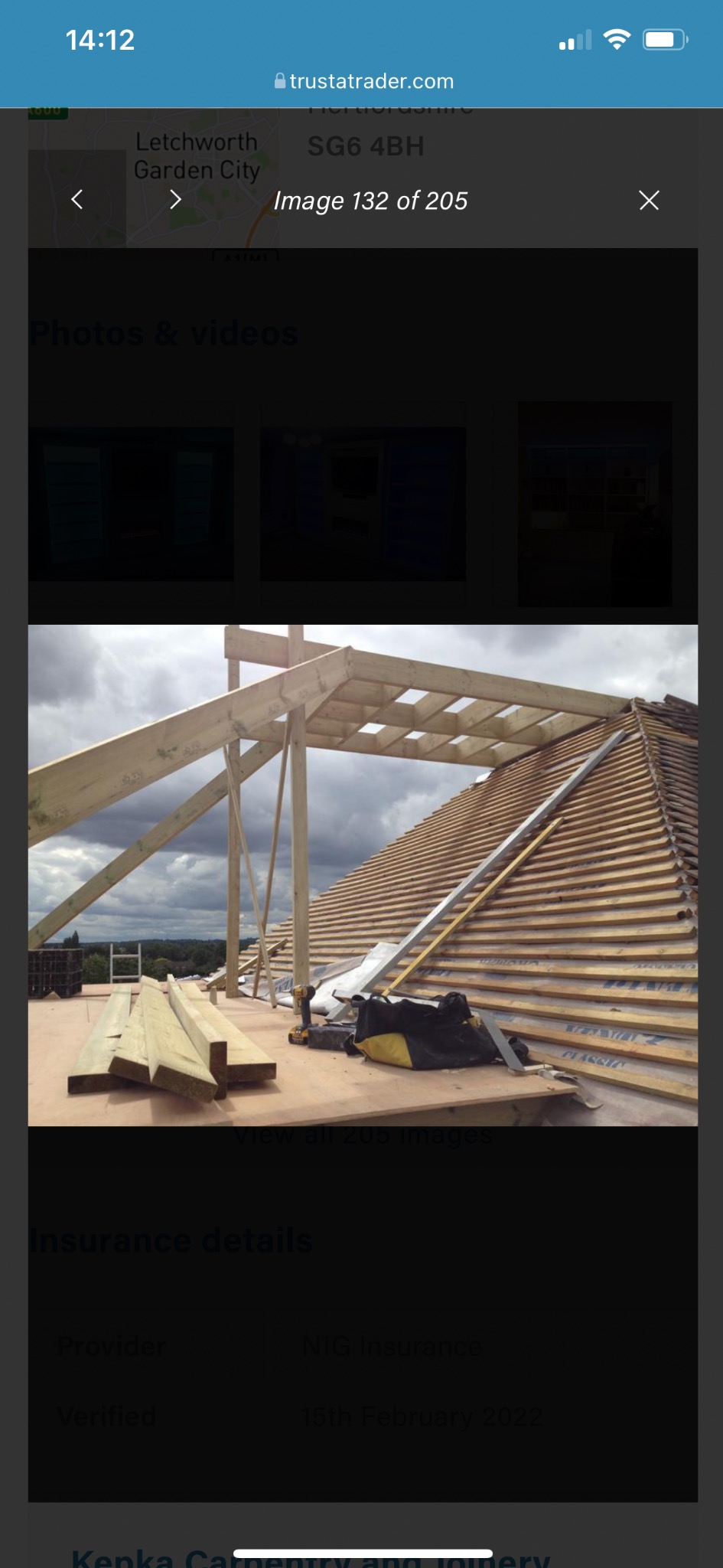 Konstrukcja drewniana dachu w trakcie budowy, widoczne krokwie, łaty, narzędzia i materiały budowlane. Tło stanowi krajobraz z zielenią i pochmurnym niebem.