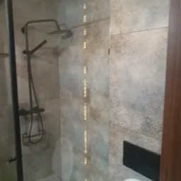 Nowoczesna łazienka z kabiną prysznicową typu walk-in, deszczownicą w kolorze grafitowym i toaletą. Płytki w odcieniach szarości z subtelnym wzorem.