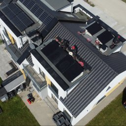 WD INSTAL - Montaż paneli słonecznych na dachu nowoczesnego domu z bliska, widok z drona. Ekipa w czarnych strojach instaluje panele, obok zaparkowany samochód z drabiną.