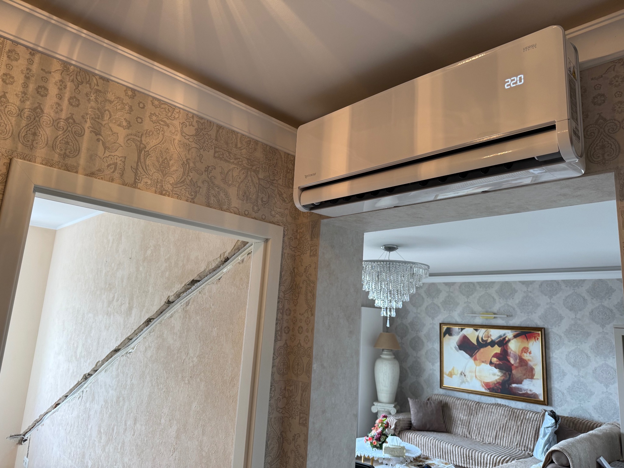 Zamontowany klimatyzator Rotenso Versu w salonie w Dominowie. Biała obudowa, wyświetlacz z temperaturą 22.0. Widoczne ozdobne tapety i fragment salonu.