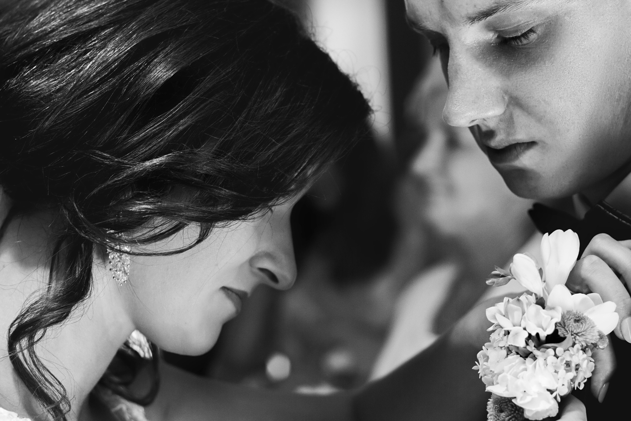 Czarno-białe zbliżenie profilu kobiety z błyszczącymi kolczykami i mężczyzny z butonierką, z delikatnym rozmyciem tła, tworzące intymną atmosferę.