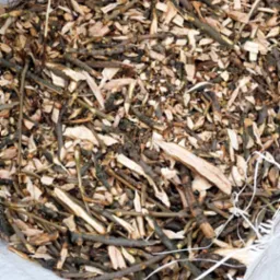 Worek wypełniony świeżo pociętymi gałęziami i drobnymi kawałkami drewna, leżący na trawie. Widoczny fragment buta osoby stojącej obok.