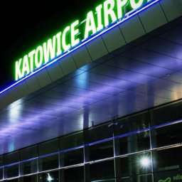 EKOTRANS-GK SPÓŁKA Z OGRANICZONĄ ODPOWIEDZIALNOŚCIĄ - Nocny widok na budynek lotniska Katowice z neonowym napisem. Szklana fasada odbija światła, tworząc nowoczesny, architektoniczny krajobraz.