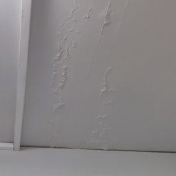 STARPLAST MARCIN KOZAKOWSKI - Z bliska widoczny biały sufit z wyraźnymi śladami zalania i uszkodzeniami. Widoczne wybrzuszenia i plamy świadczą o przecieku. Oświetlenie sufitowe w lewym górnym rogu.