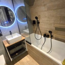 Sperbud - Nowoczesna łazienka z beżowymi płytkami imitującymi drewno, czarną armaturą i okrągłymi lustrami z podświetleniem LED. Umywalka nablatowa z szafką.