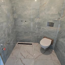 Sperbud - Wykończona łazienka z marmurowymi płytkami w odcieniach szarości i bieli. Widoczna toaleta, odpływ liniowy i armatura. Minimalistyczny design, jasne oświetlenie.