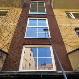 ProClean+ Kamil Pruchniewicz - Wysokie okna w kamienicy myte teleskopową szczotką z dołu. Na elewacji widoczne pnącza. W oknach odbija się budynek po przeciwnej stronie ulicy.