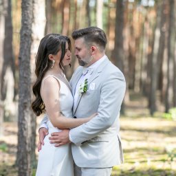 Wioletta Pietrucha Fotografia - Para młoda w jasnych strojach, obejmująca się czule w zalesionym plenerze. Delikatne światło podkreśla naturalność scenerii i intymność chwili.