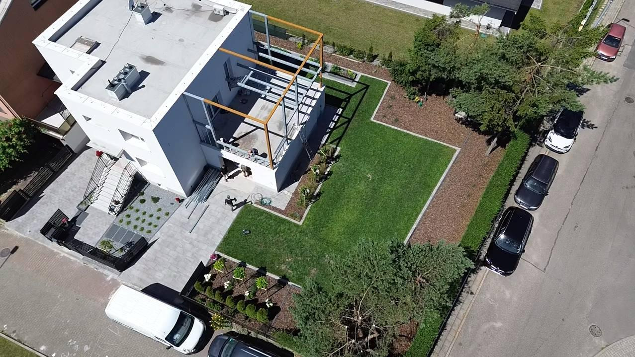 Nowoczesny dom z płaskim dachem i minimalistycznym ogrodem, widok z drona. Elementy drewniane pergoli, równo przystrzyżony trawnik i geometryczne rabaty.