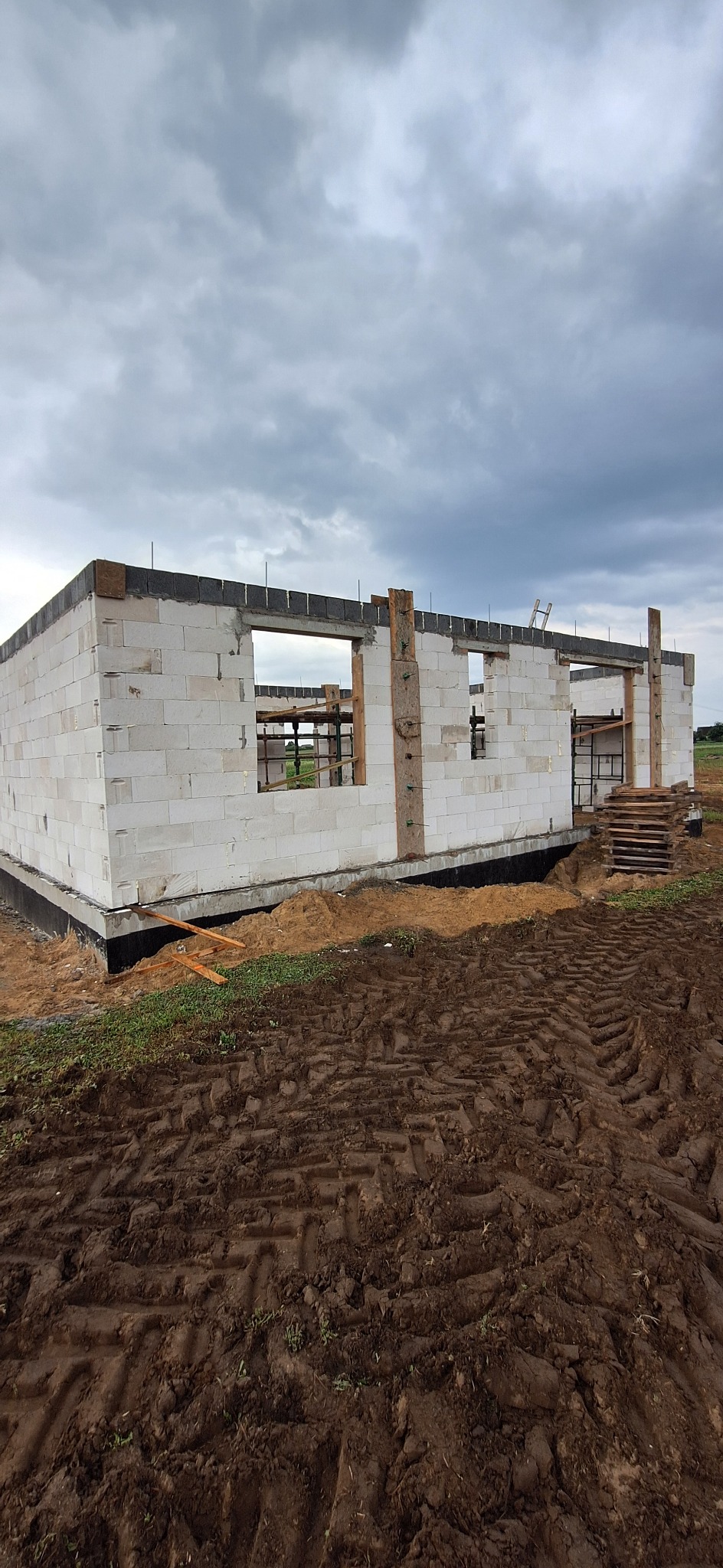 Budowa domu z białych bloczków w Bolewicach, widoczne fundamenty i ściany w stanie surowym otwartym, szare niebo w tle.