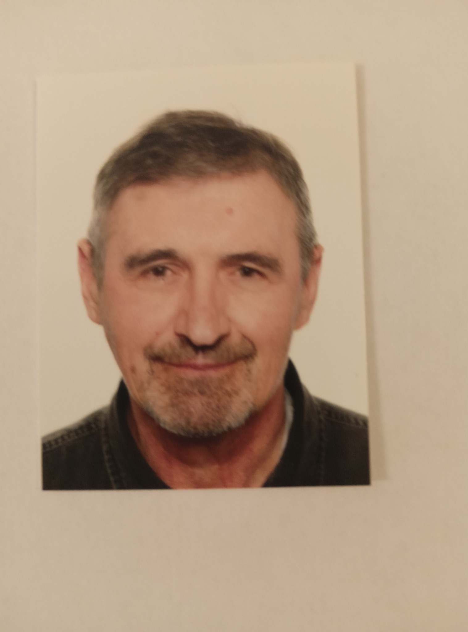 Portret mężczyzny z lekkim uśmiechem, brodą i wąsami. Zdjęcie na białym tle, oświetlenie naturalne, z delikatnym cieniem.