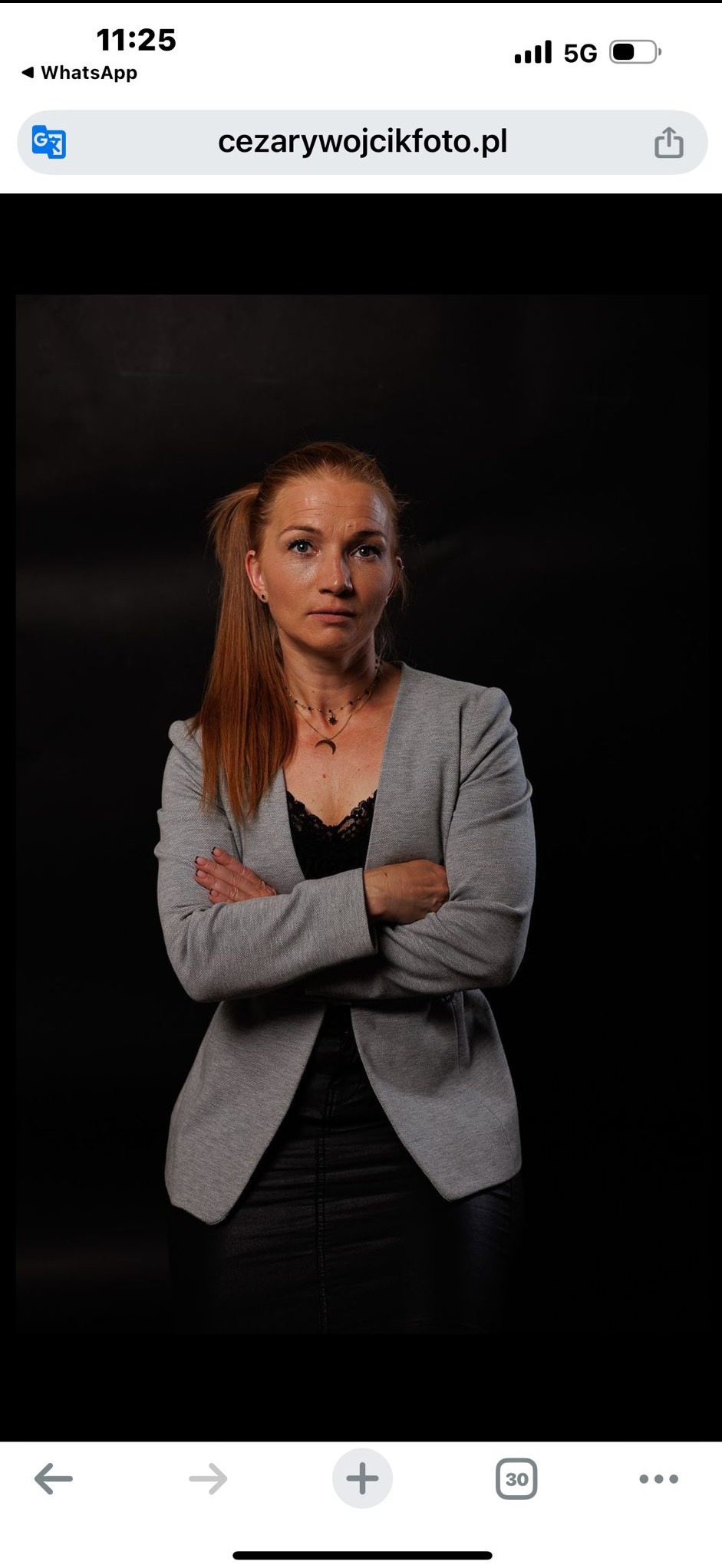 Portret kobiety w szarym żakiecie na czarnym tle, z rękami skrzyżowanymi, sugerujący profesjonalizm i pewność siebie, idealny na profil trenera personalnego.