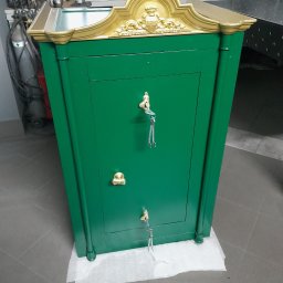 Rafał Macina - Zielony, metalowy sejf z ozdobnym, złoconym wykończeniem, stojący na podłodze wyłożonej szarymi płytkami. Widoczne narzędzia w tle.