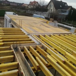 Mi-Mex - Szczegółowy widok szalunku stropowego z żółtymi belkami i stalowymi prętami zbrojeniowymi na budowie domu jednorodzinnego w pochmurny dzień.