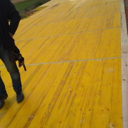 Mi-Mex - Żółte płyty szalunkowe na fundamencie w Pińczowie, częściowo widoczna sylwetka pracownika z narzędziami, w tle dom jednorodzinny i krajobraz.