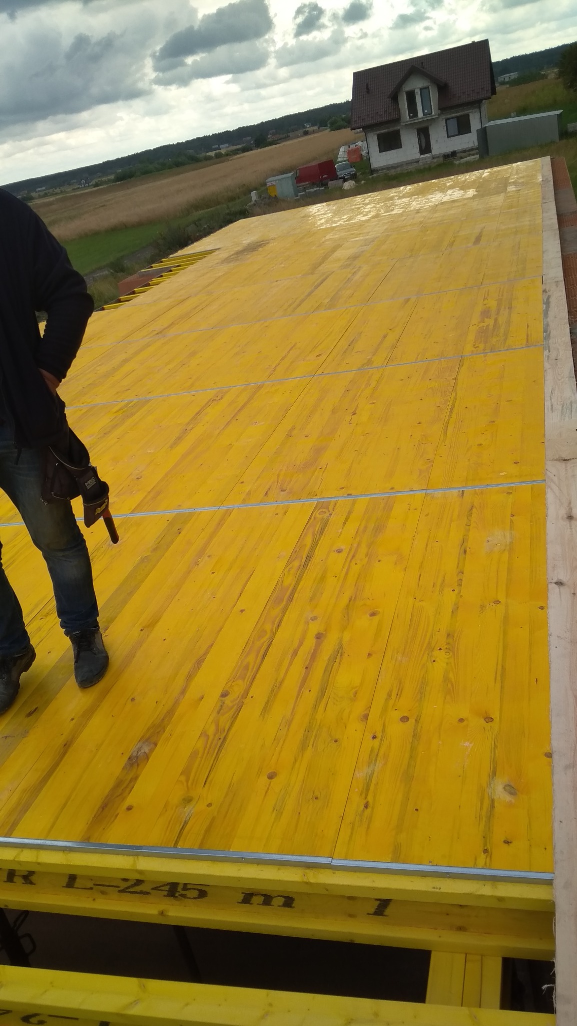 Żółte płyty szalunkowe na fundamencie w Pińczowie, częściowo widoczna sylwetka pracownika z narzędziami, w tle dom jednorodzinny i krajobraz.