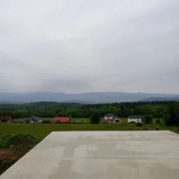 Wylana płyta fundamentowa pod budowę domu na tle zielonych wzgórz i lasów. Widok na krajobraz w pochmurny dzień.