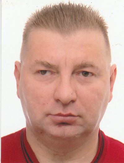 Portret mężczyzny o krótkich włosach, ubrany w czerwoną koszulkę, na jasnym tle. Ujęcie od przodu, skupione na twarzy.