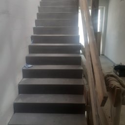 GL House Sp. z o.o. - Surowe, betonowe schody w trakcie budowy, widoczne drewniane podpory, ściany w stanie surowym. Kąt ujęcia od dołu, ukazujący perspektywę schodów w górę.