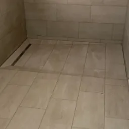 Nowoczesna kabina prysznicowa z beżowymi płytkami i odpływem liniowym, minimalistyczny design, neutralna kolorystyka.