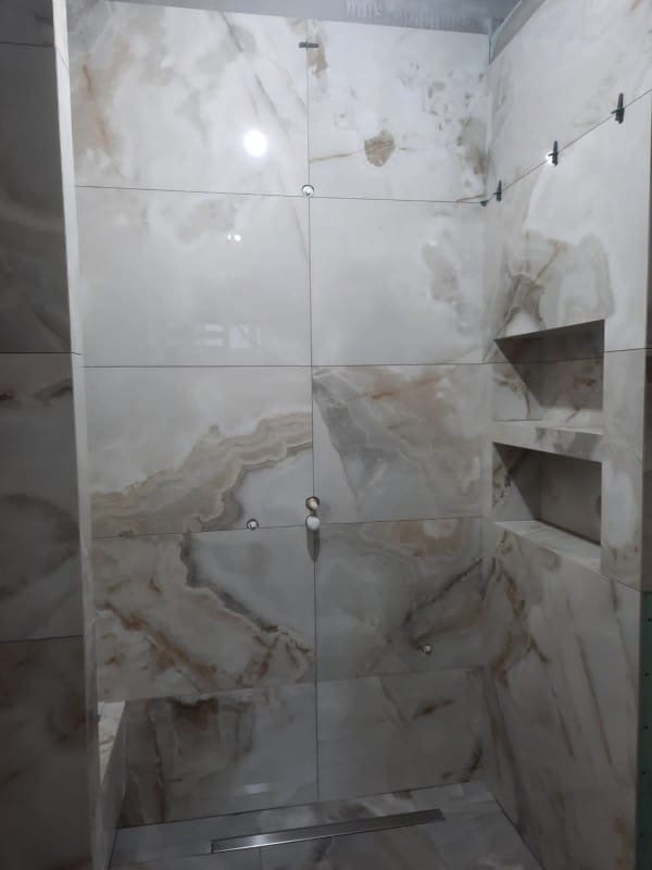 Wykończona kabina prysznicowa z beżowo-białymi płytkami imitującymi marmur, z wnękami na kosmetyki i odpływem liniowym w podłodze.